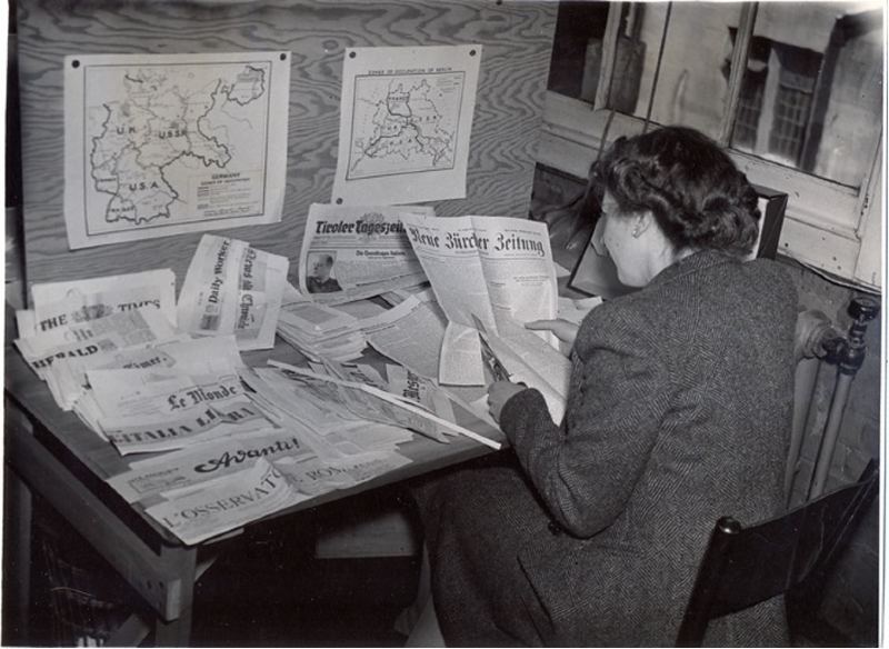 A women photographed from behind and sat at a desk with papers.