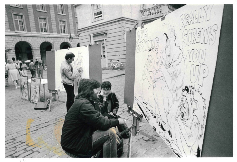 People outside in a square with various posters/drawings on display.