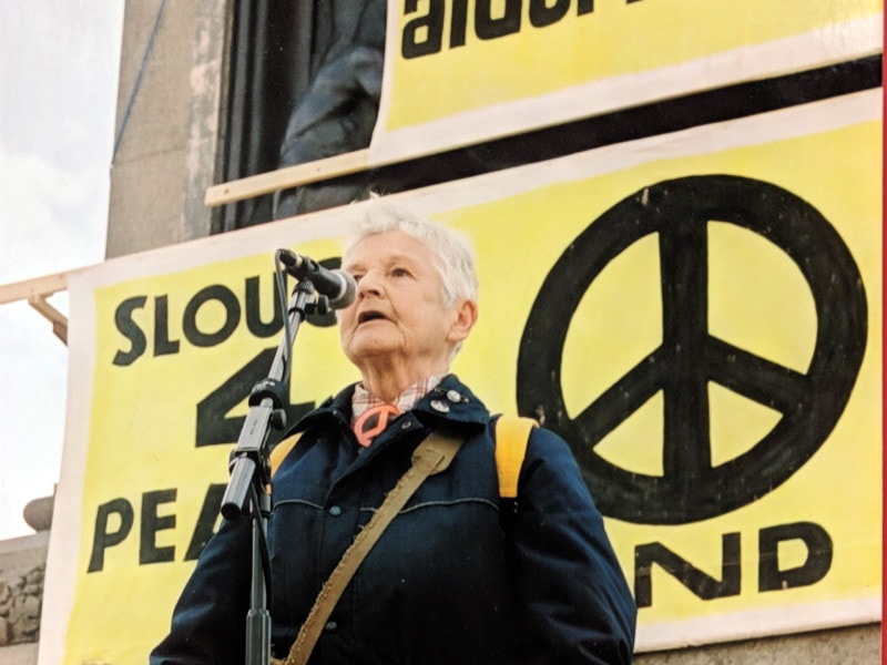 A woman talking at a microphone in front of a CND banner