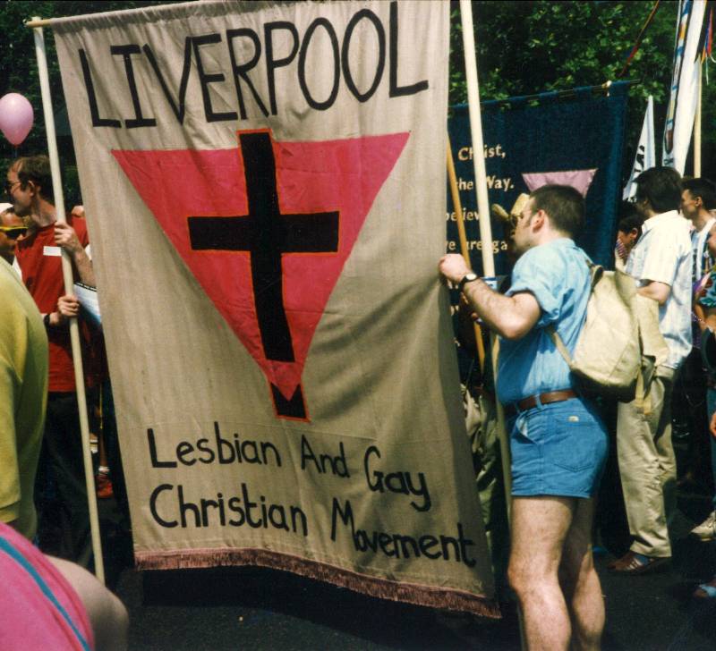A colour photo of a march. Includes a large banner with 'Liverpool' written on it and 'Lesbian and Gay Christian Movement'.