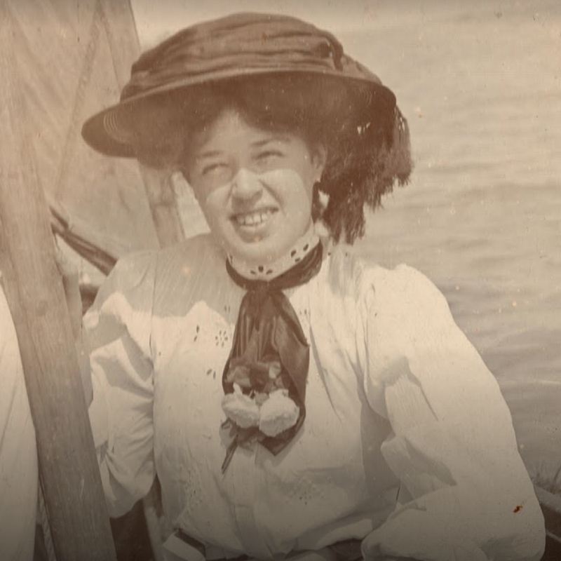 Vera 'Jack' Holme sat on a boat wearing a bonnet and smiling at the camera