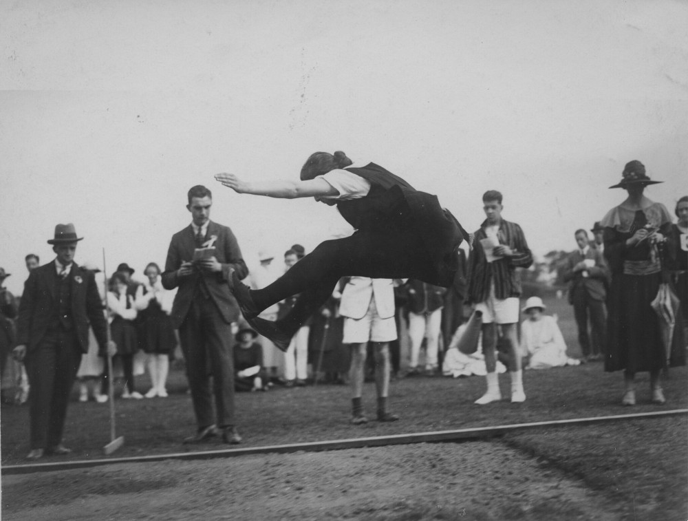 A person captured in mid-air doing a long jump. People are looking on.