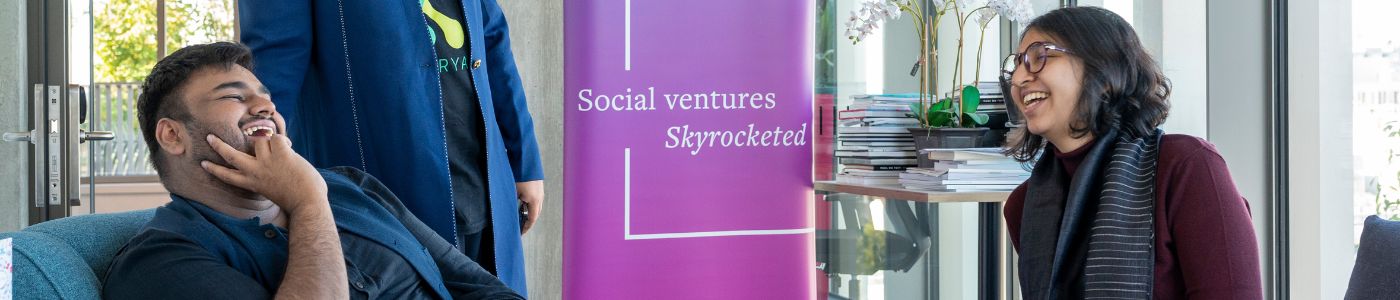 Two ventures chatting together smiling in front of a 100x banner that reads social ventures skyrocketed