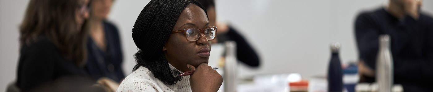 Woman sitting in a classroom with her hand on her chin in thought.