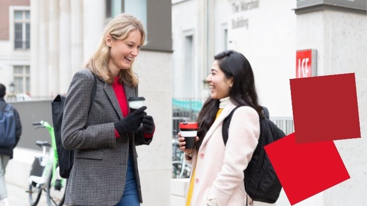 Two female students outside the Marshall Building smiling and drinking takeaway coffee