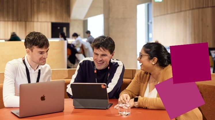 Group of students smiling working at a table on laptops