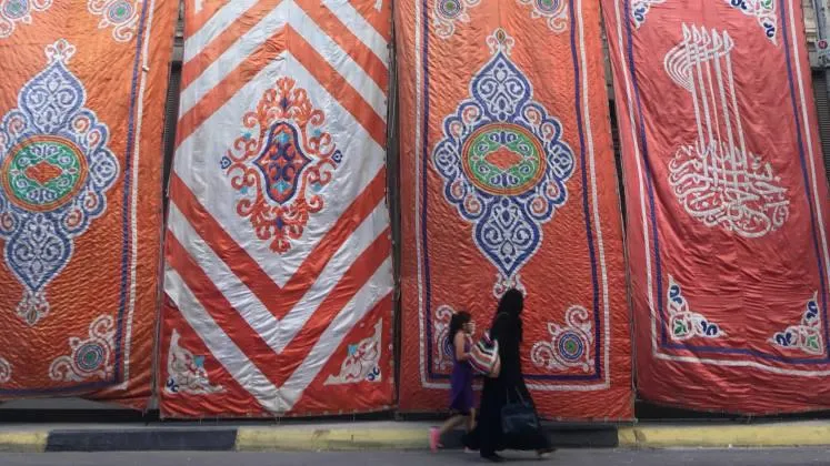 A women and a young girl walking in front of large, colourful textiles in Cairo.