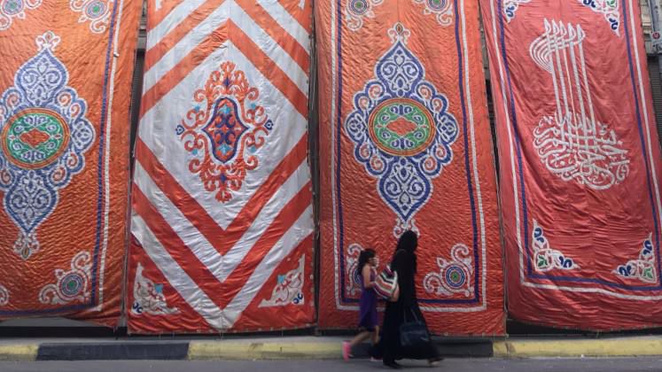 Two women in Egypt walking past a background of patterned fabric