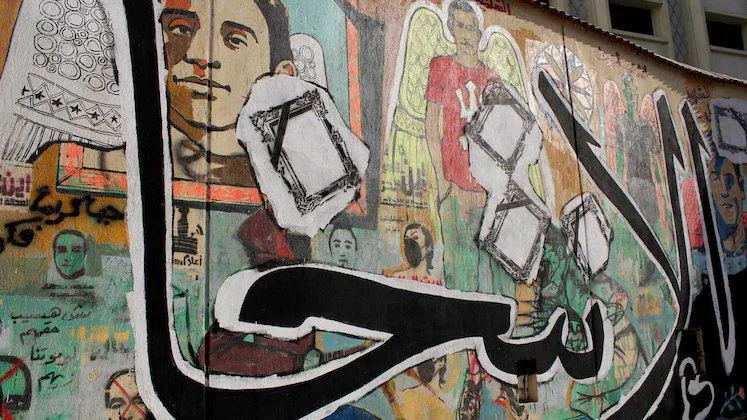 Graffiti mural with layers of portrait images and Arabic text