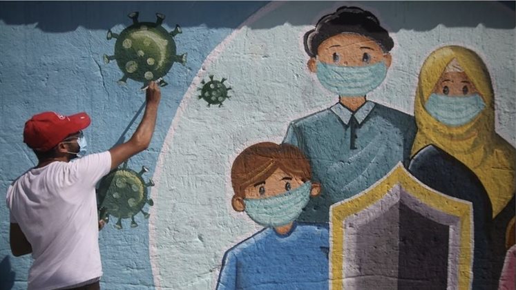 Mural painted in Gaza of a family in masks and cartoon covid virus framing the outside of the mural. 