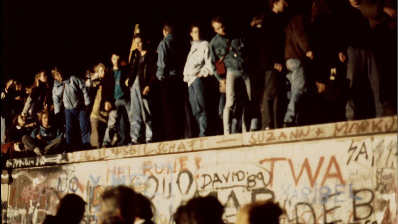 People stand on the Berlin Wall, covered in graffiti