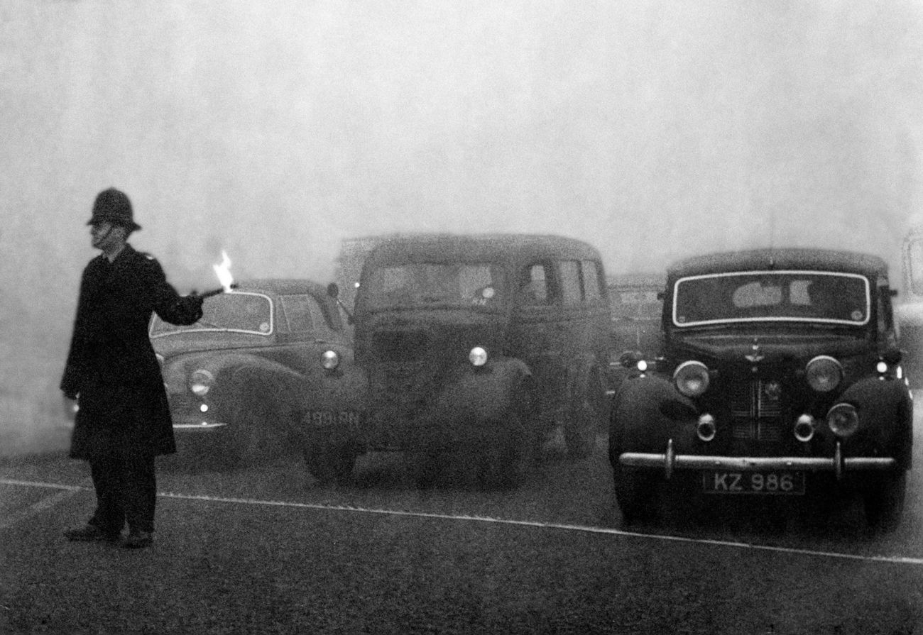 A policeman guides traffic with flare in London's Great Smog