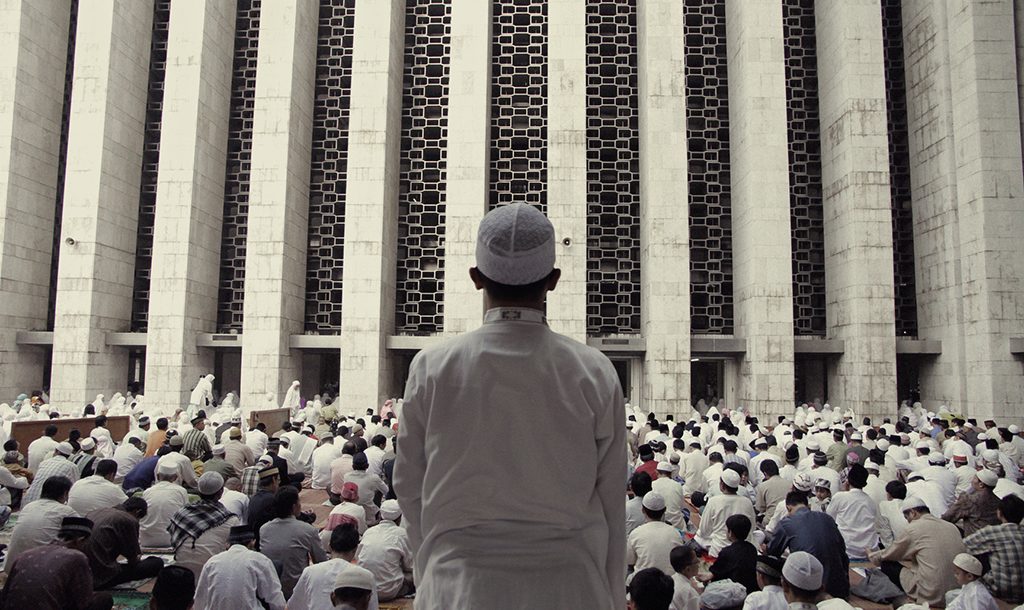 A man standing in front of an Indonesia mosque's facade behind a crowd of worshippers