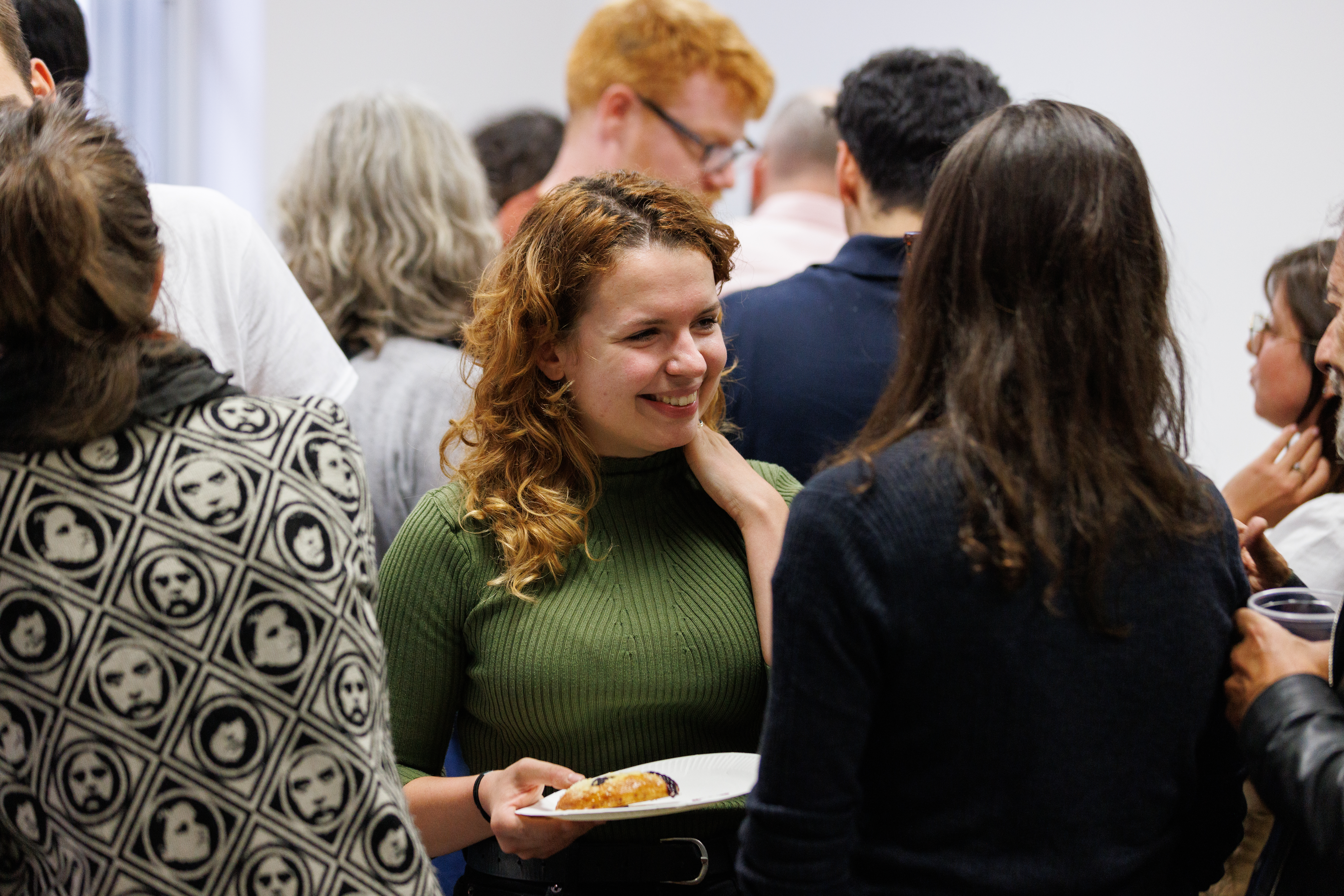 A smiling PhD student in conversation with an other student. In the background, other faculty and PhD students can be seen.