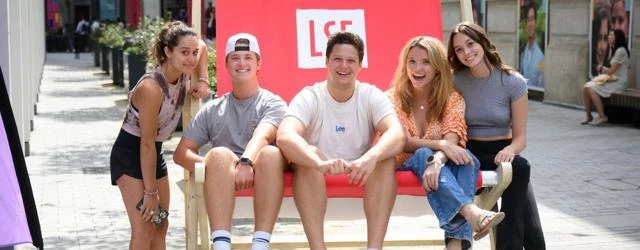 A group of five students sitting on a very large LSE branded deck chair