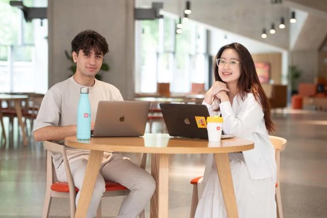 Two students sat at table in Marshall Building with laptops