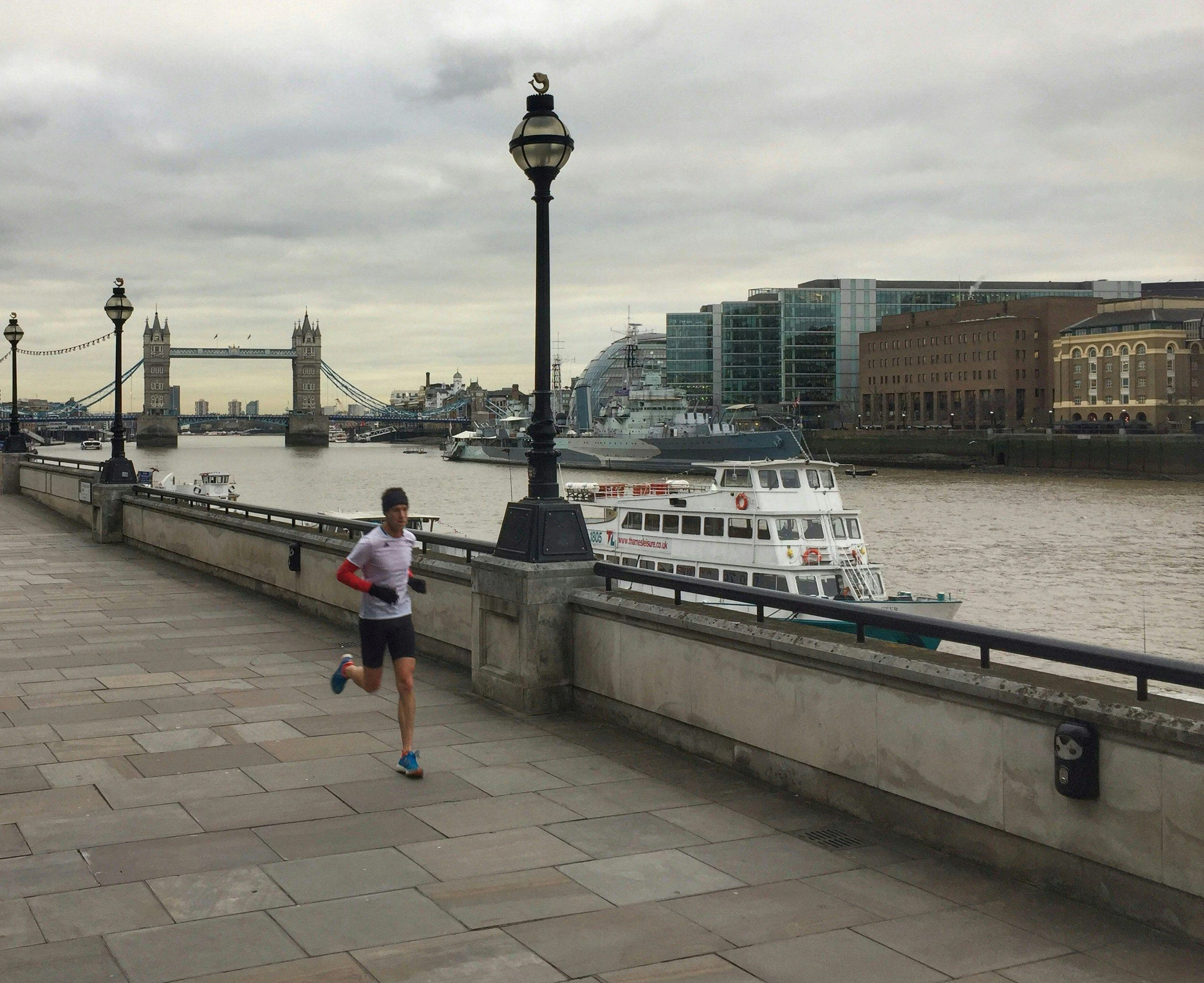 Lone male runner, runs along Thames path, view of London Bridge in background