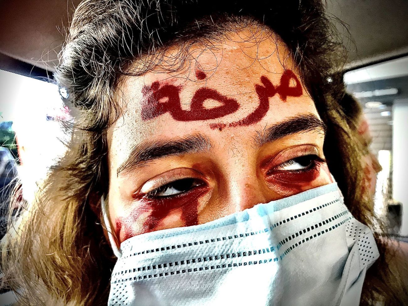A person wearing a face mask with red writing on their forehead 