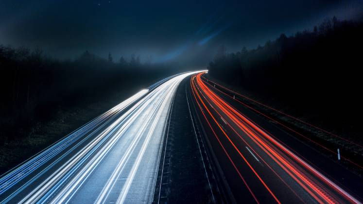 White and red lights from cars stream across a landscape in the darkness