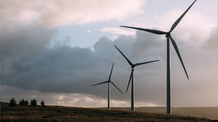 Three windmills stand in a row against the backdrop of a cloudy sky