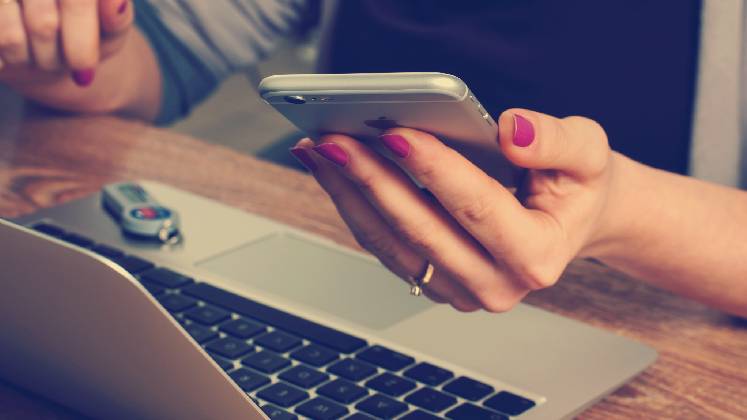 A woman sitting at her laptop picks up her phone