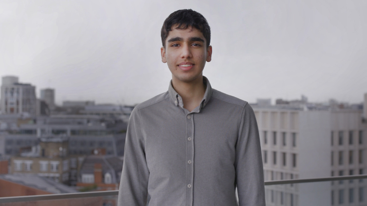 A male scholarship recipient stands on the CKK terrace with the Marshall Building visible in the background